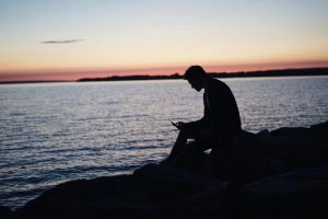 silhouette d'un homme assis au bord de la mer au crépuscule