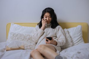 photo d'une fille assise sur son lit qui pleure en regardant son smartphone